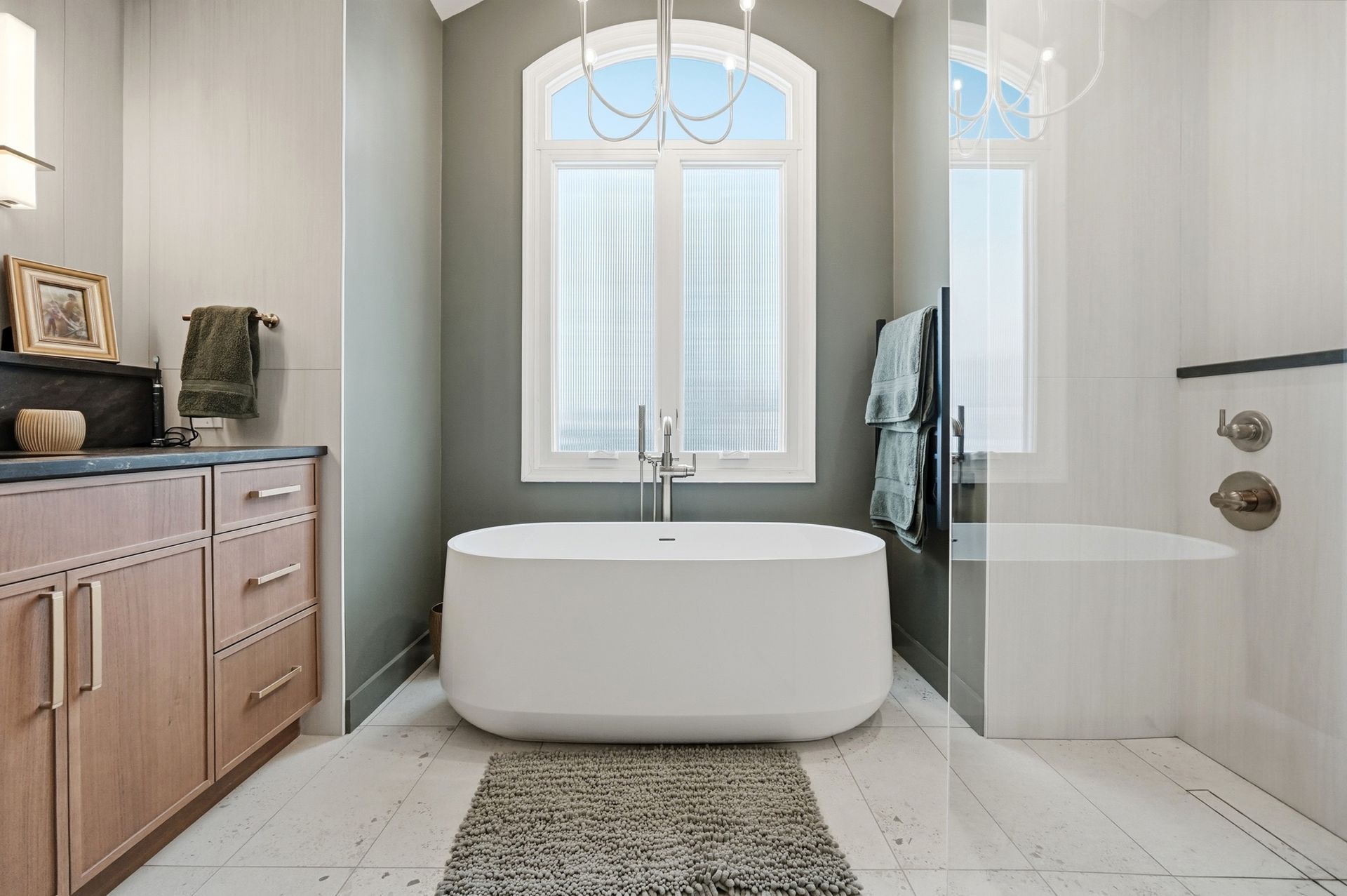 Bathroom with a white freestanding tub centered in front of a window. Light wood cabinets on the left.