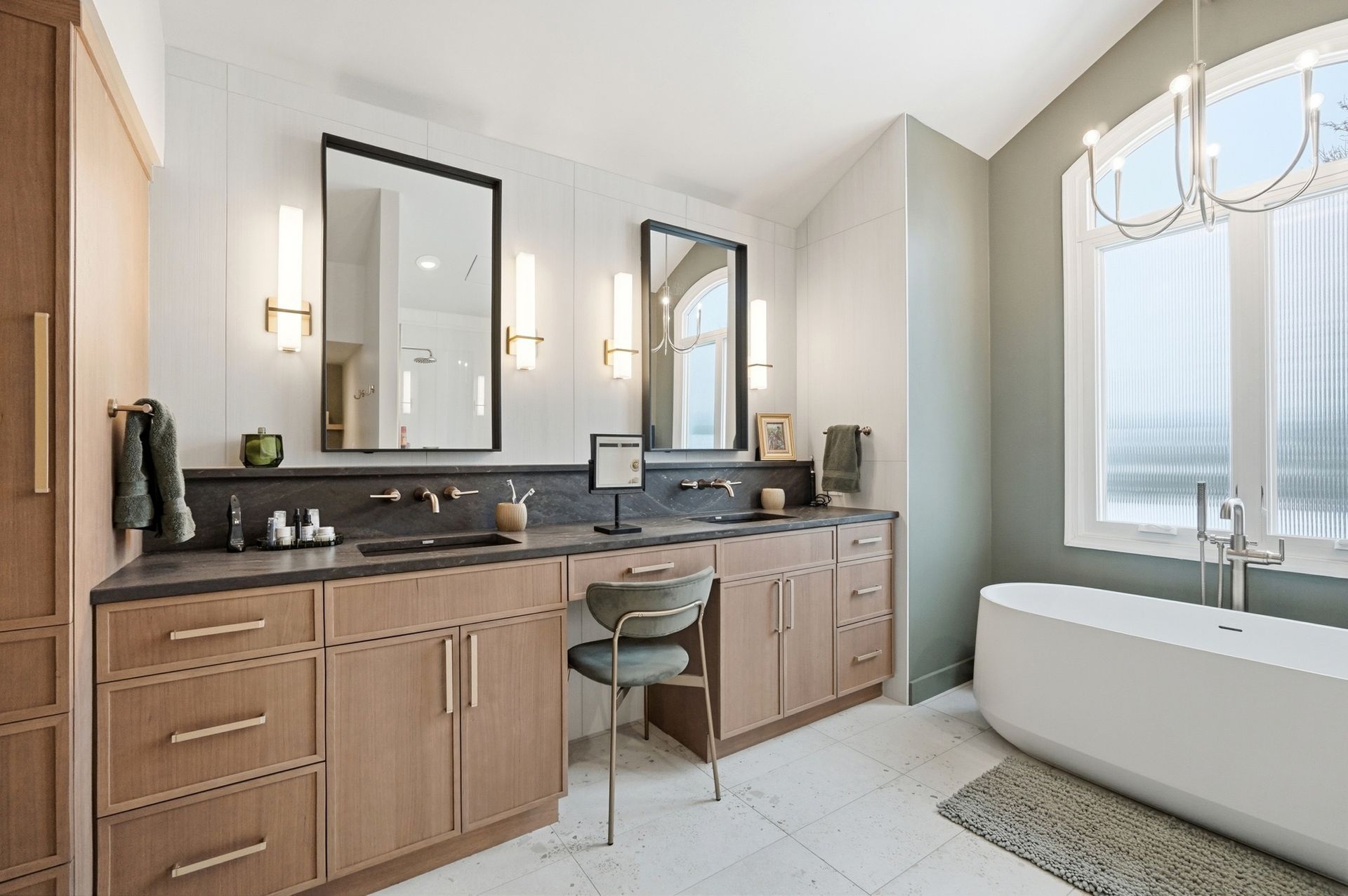 Bathroom with wooden cabinets, dark countertops, two mirrors, and a freestanding tub.