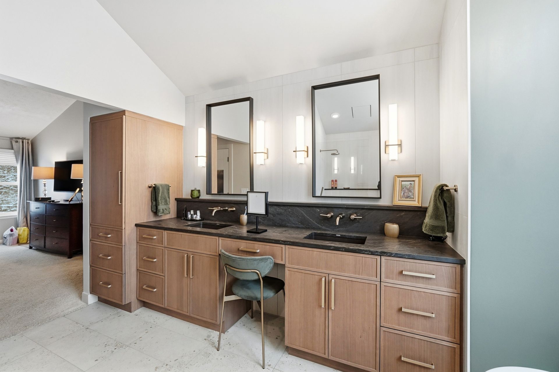 Bathroom with double vanity, two mirrors, and a tall cabinet. Light wood cabinets, black countertops.