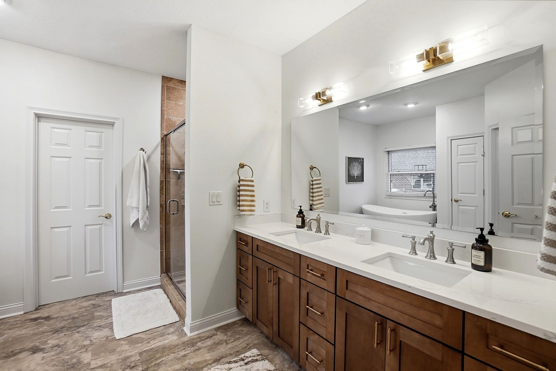 Bathroom with wood cabinets, white countertops, double sinks, large mirror, and glass shower.