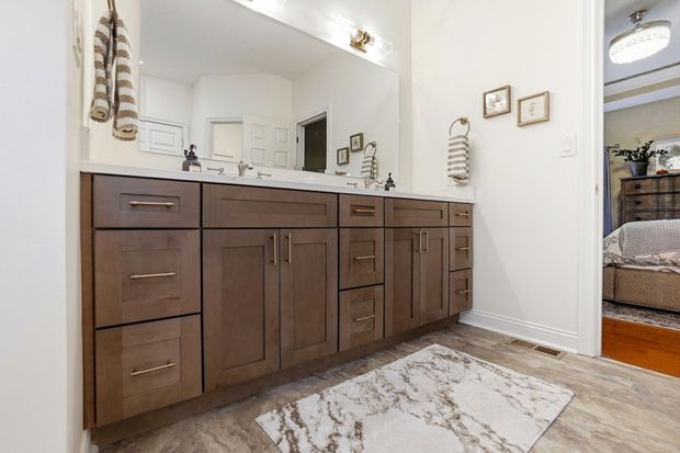 Bathroom with a brown vanity, double sinks, and a large mirror. A rug sits on the floor.
