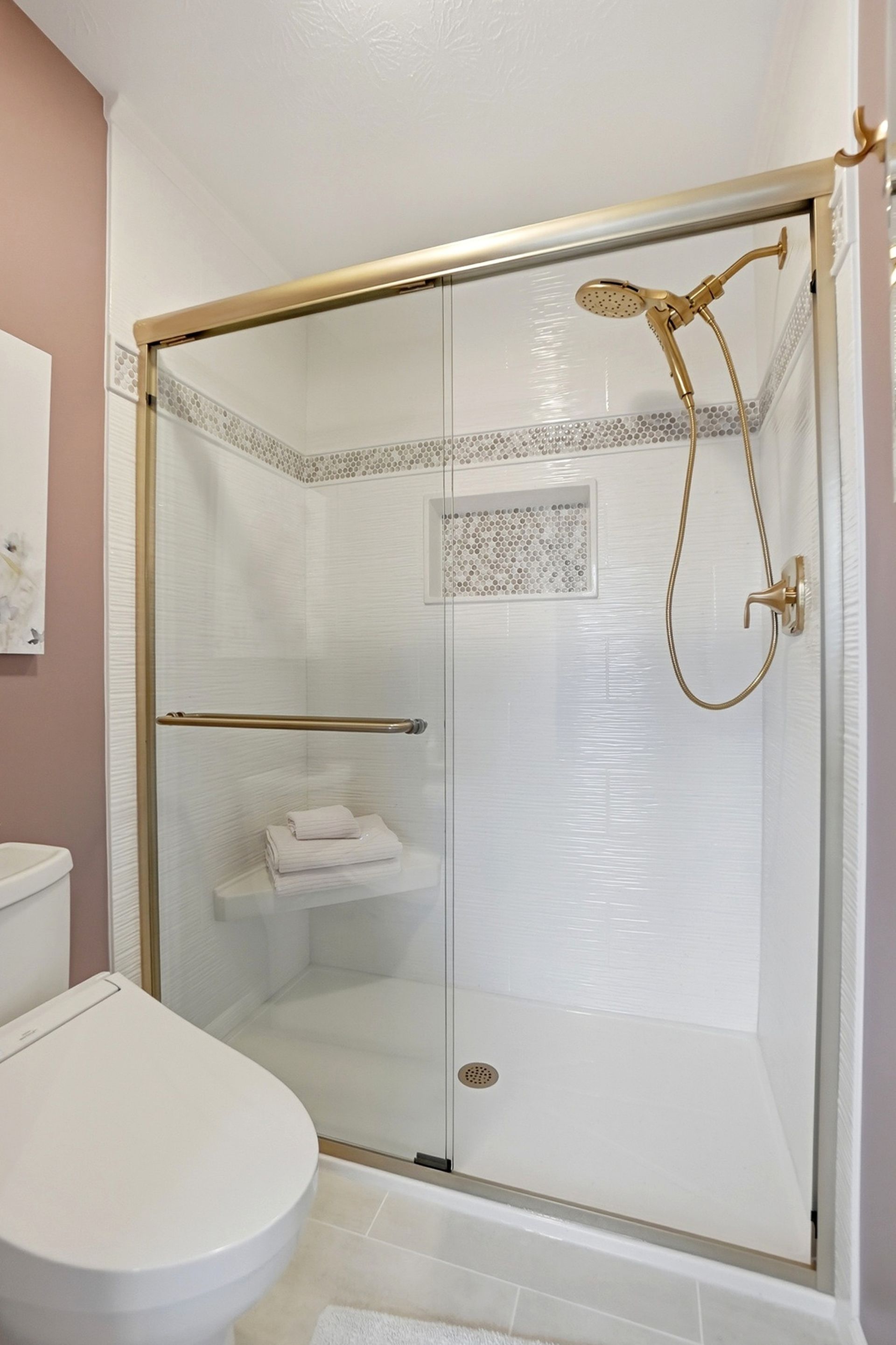 Bathroom with a gold-framed glass shower, white toilet, and pink wall.