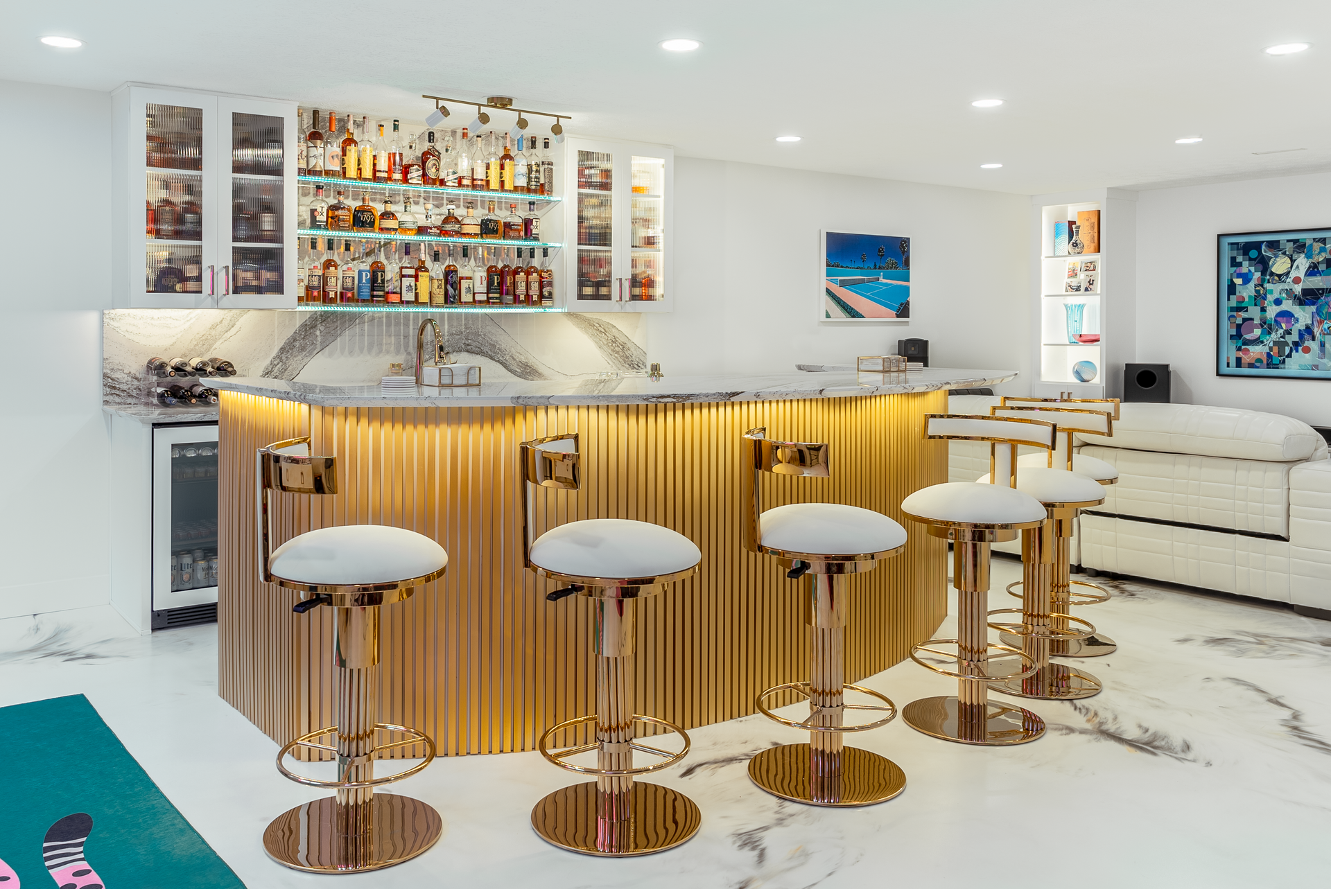 A luxurious home bar with gold accents, white stools, and a well-stocked liquor display.