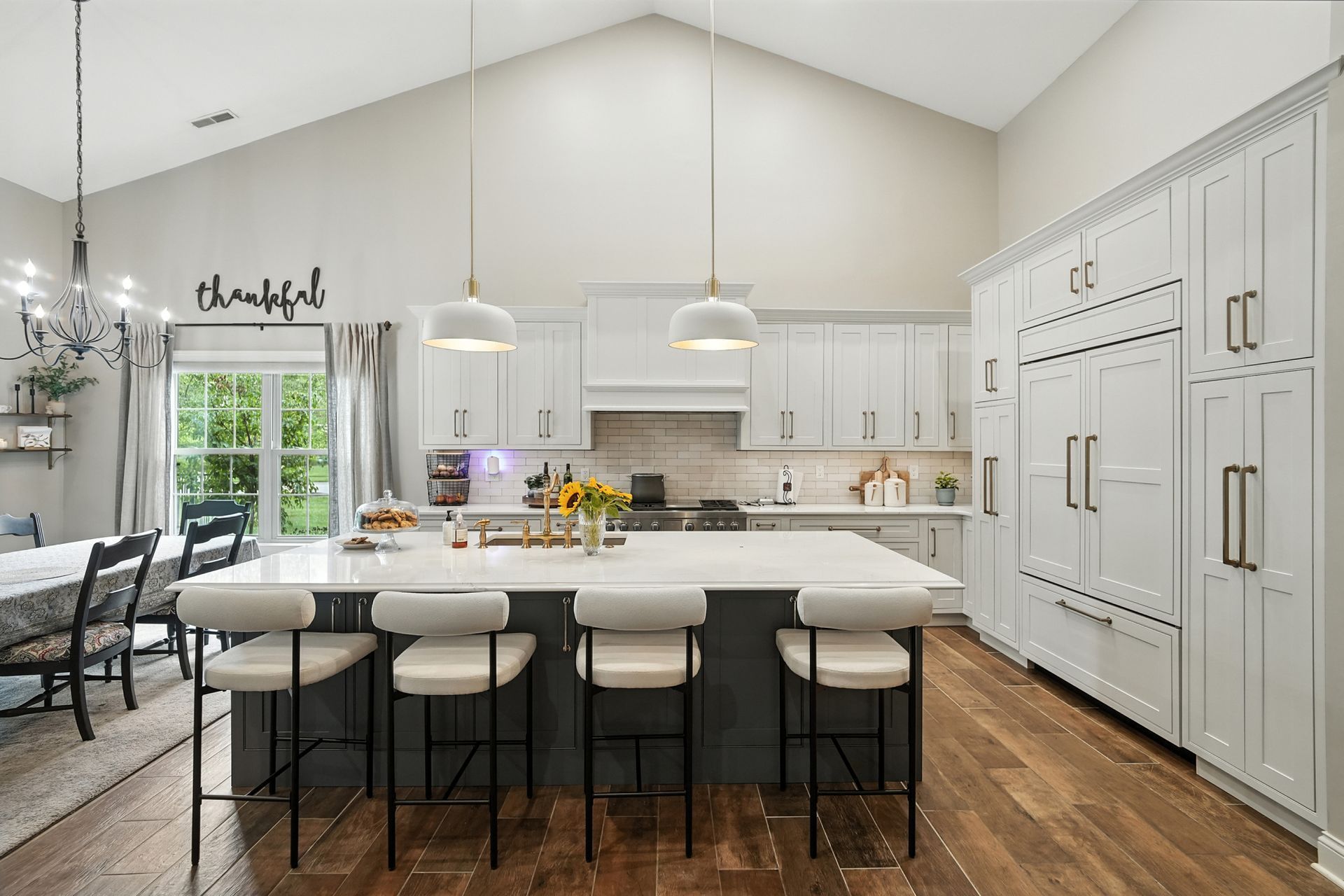 Modern kitchen with white cabinets, island, and wood floors. Dining area with chandelier visible.