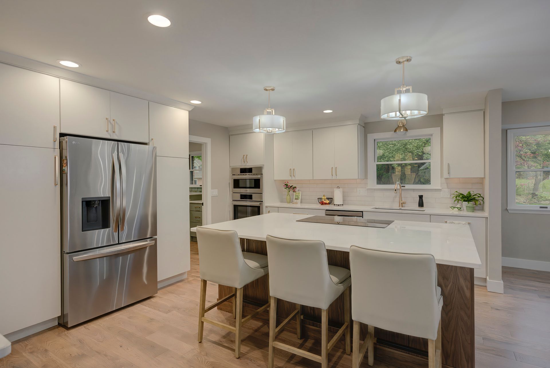 Modern kitchen with a large island, stainless steel refrigerator, and light wood floors.