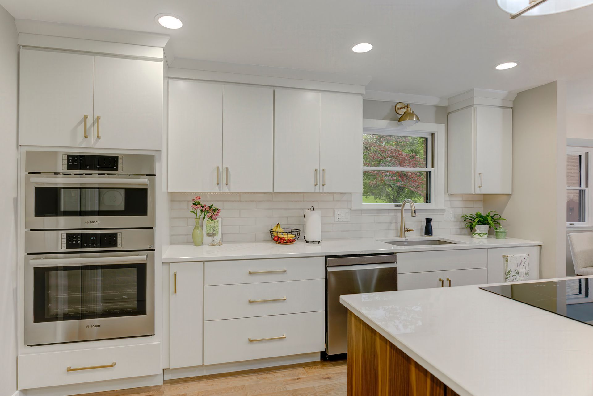 White kitchen with built-in ovens, white cabinets, stainless steel appliances, and a quartz countertop.