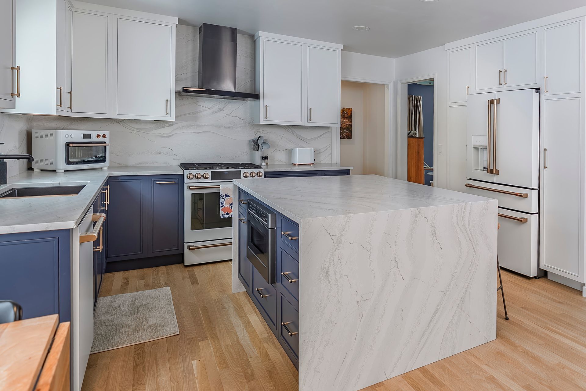Kitchen with white and blue cabinets, marble island and countertops, stainless steel appliances, and wood floors.