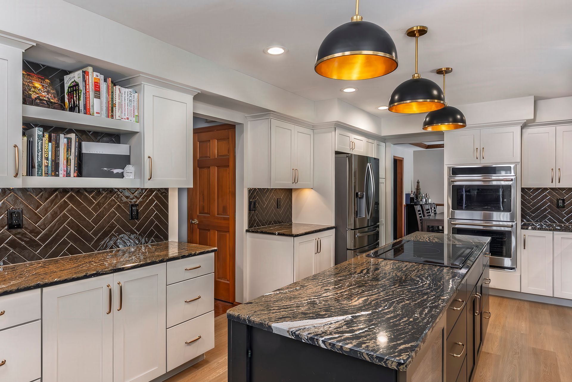 Modern kitchen with white cabinets, dark island, gold and black pendant lights, and herringbone backsplash.