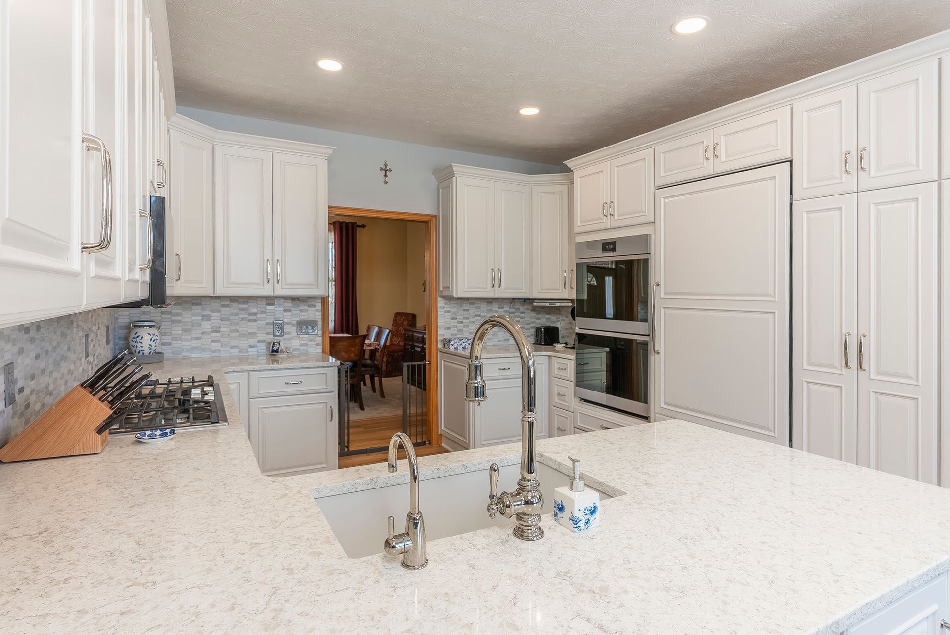 White kitchen with cabinets, island, and stainless steel sink. Doorway to another room visible.