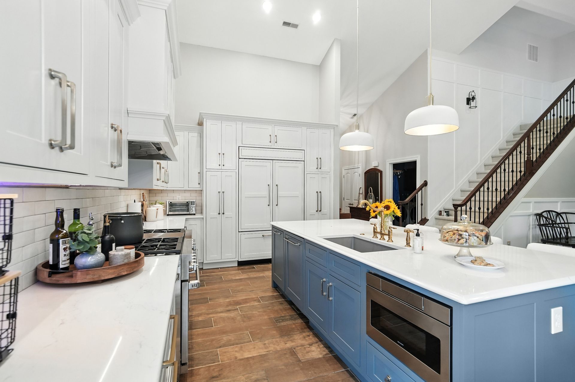 Kitchen with white cabinets, blue island, stainless steel appliances, and wood floor.
