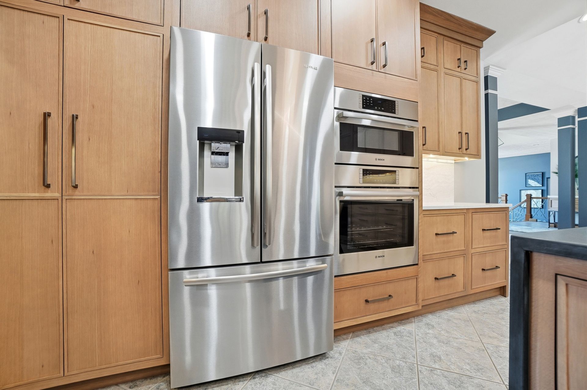 Stainless steel refrigerator and oven in a kitchen with light wood cabinets.