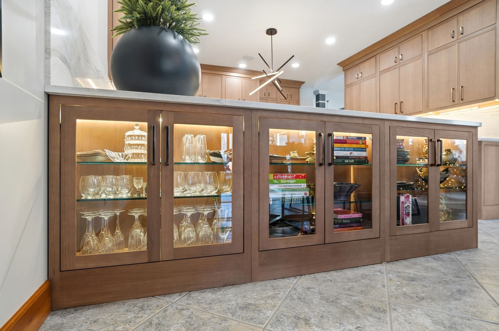 Wooden cabinet with glass doors, displaying lit glassware and decor.