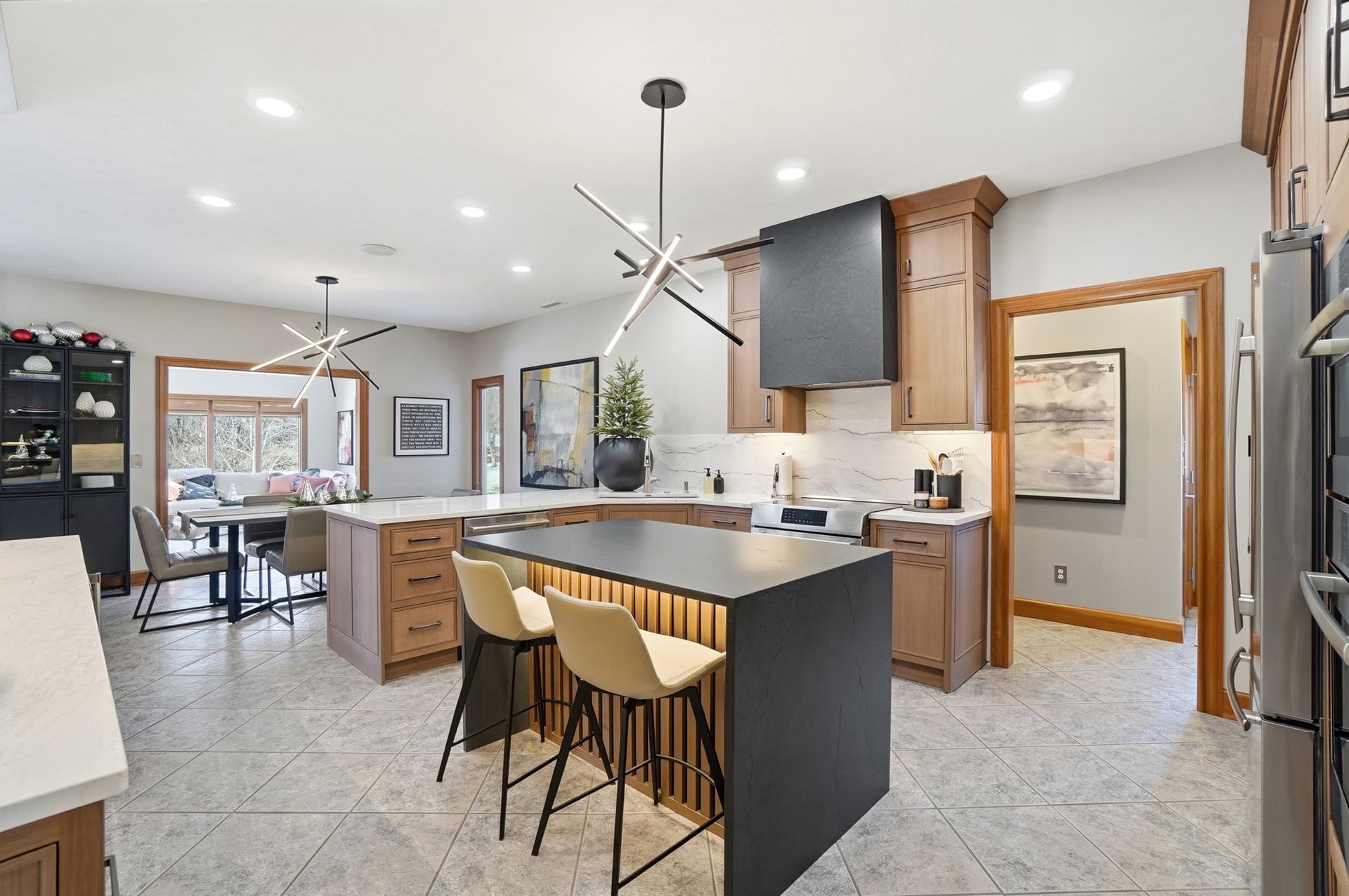 Modern kitchen with brown cabinetry, black island, light-colored countertops, and pendant lights.
