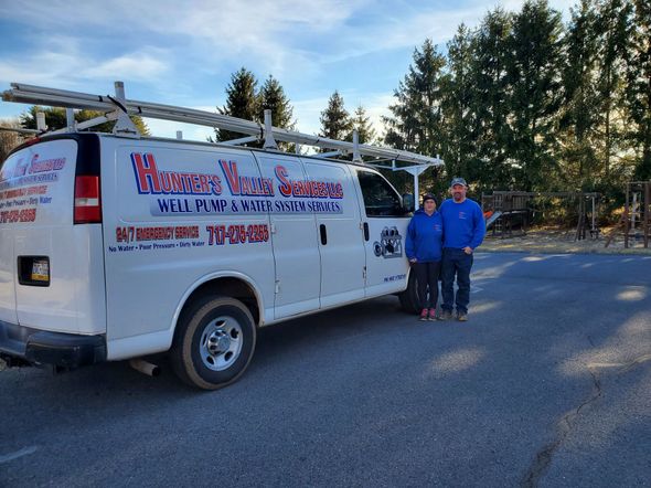 Blue water pump system with tank, pipes, and electrical box on concrete pad.