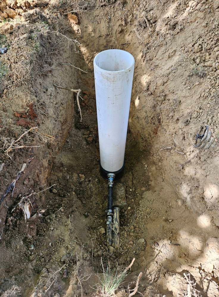White pipe extending from soil, connected to a cable, in a dirt trench.