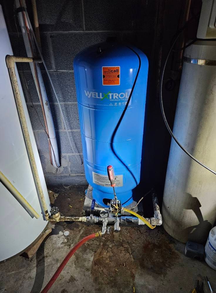 Blue well water tank in a basement with pipes and other equipment.