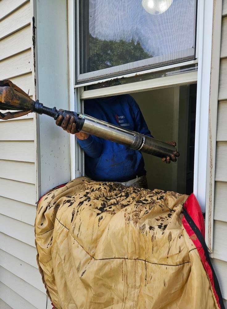 Person in blue shirt holding a metal object out of a window, above a brown tarp.