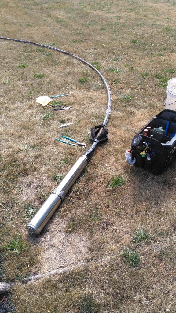 Well pump and electrical cable on grass, tools nearby.