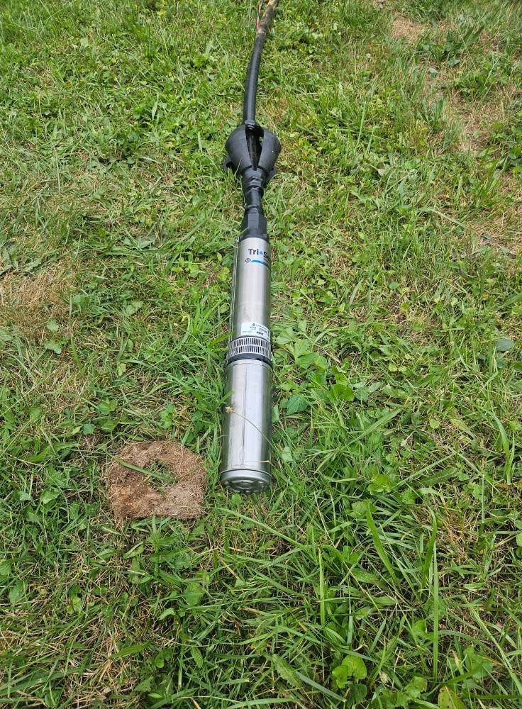 Silver submersible well pump on green grass.