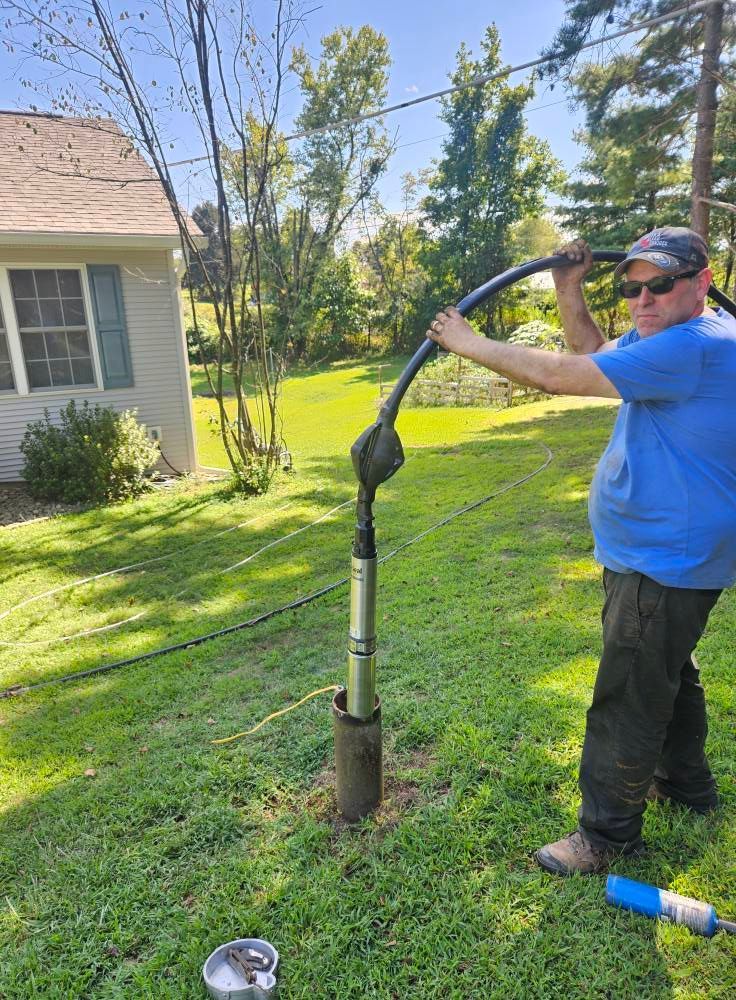 Man in blue shirt works on well in grassy yard.