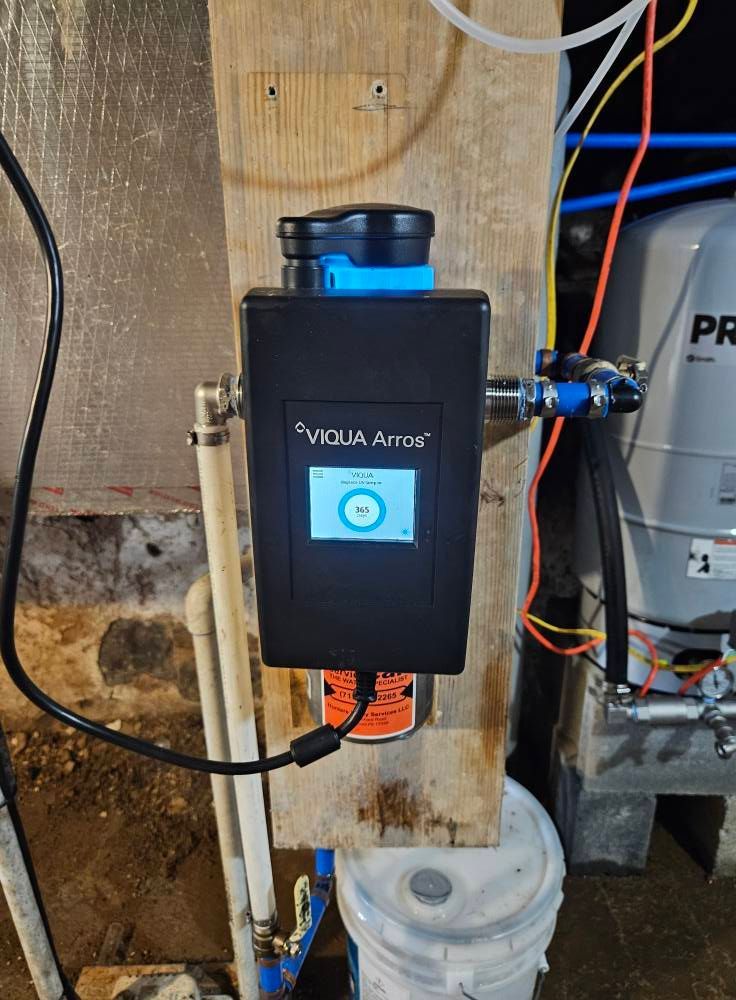 A water system monitor attached to a wooden board, with pipes and a tank visible.