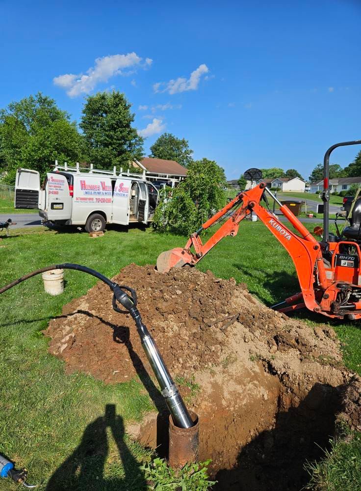 Orange excavator digging in a yard, near a van with company logos and buried cable.
