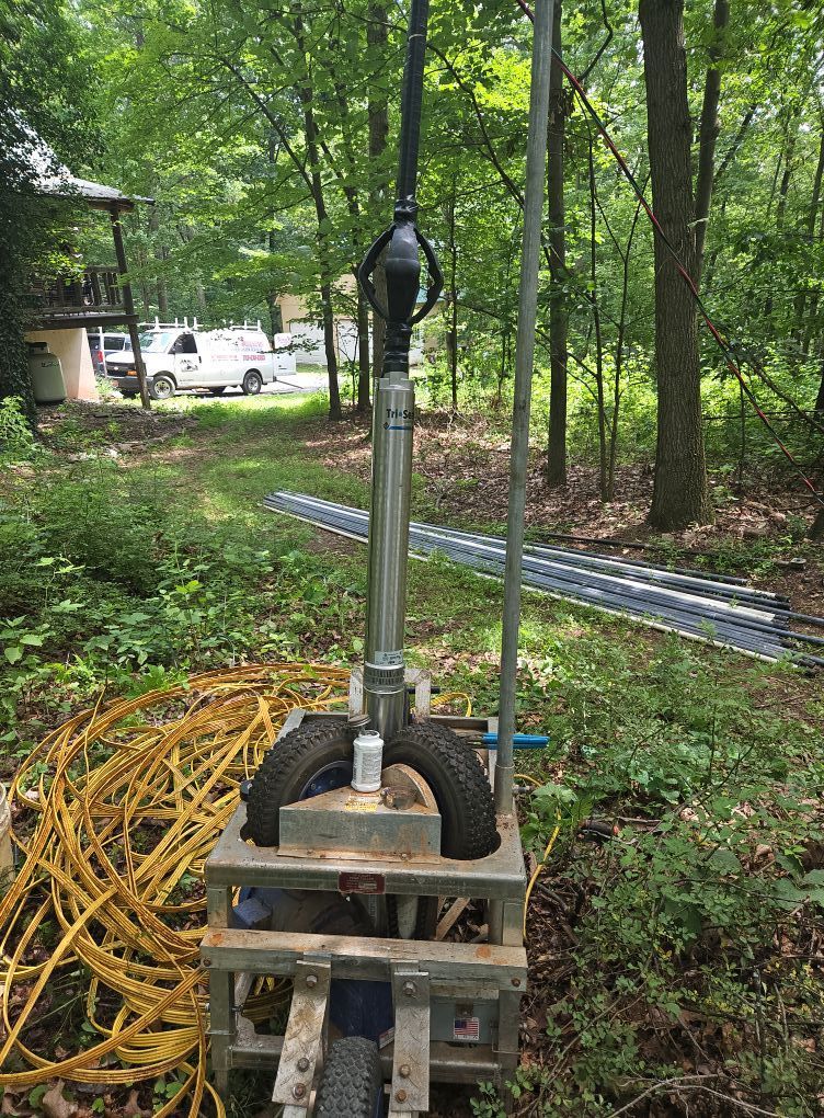 Well drilling machine, outdoors in woods, with pipes and hoses.