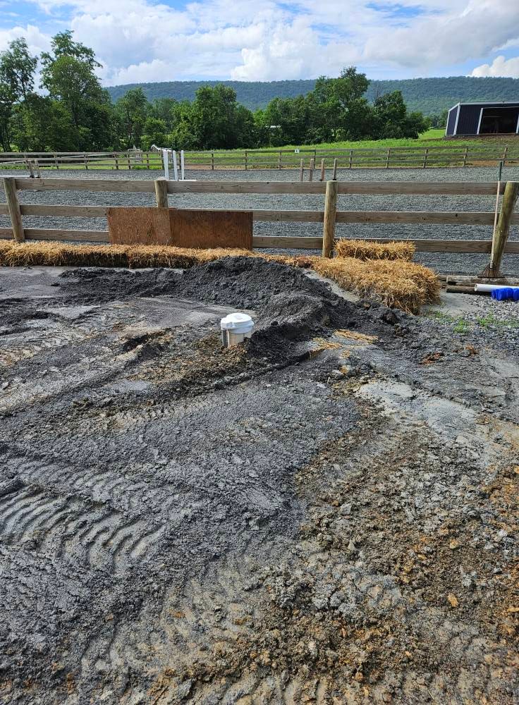Earthen horse arena under construction with visible fencing and mountains in the background.