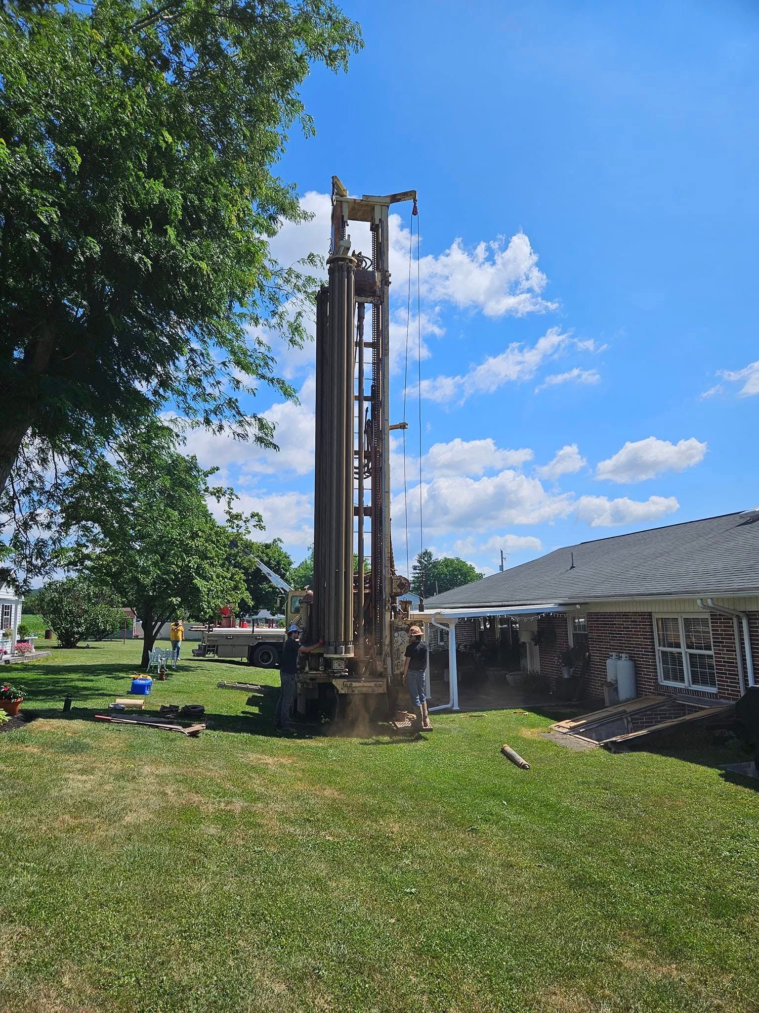 Drilling rig set up on a lawn next to a house under a partly cloudy blue sky.