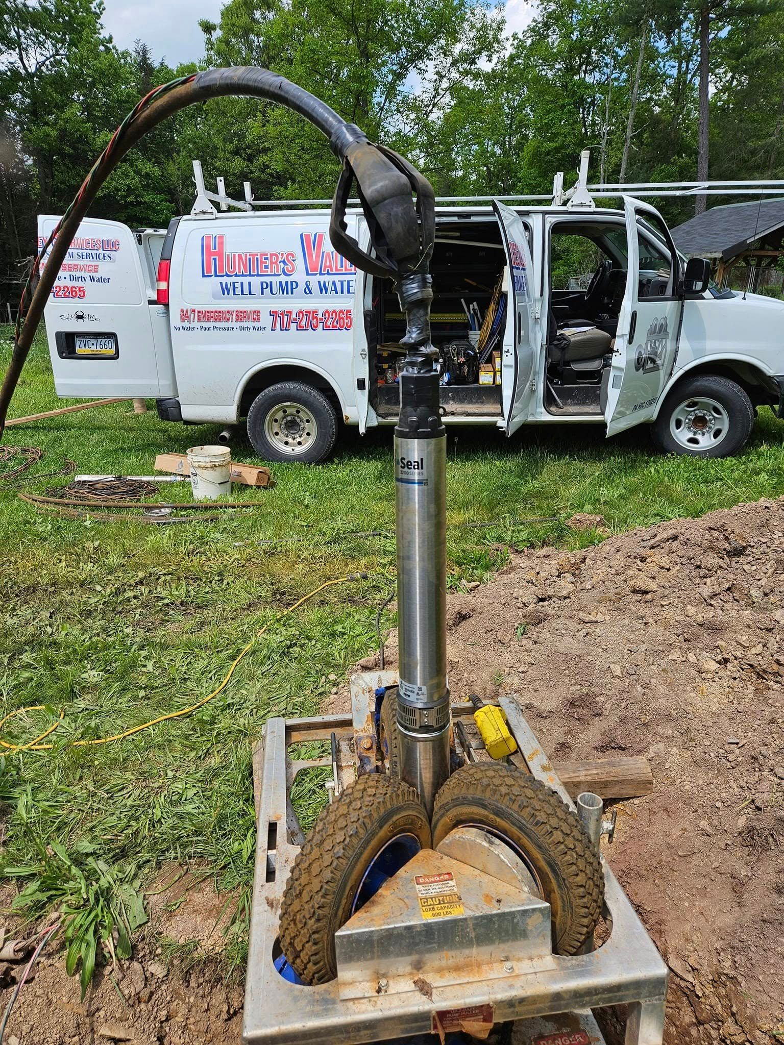 Well pump assembly with vehicle in the background. It is outdoors on grass.
