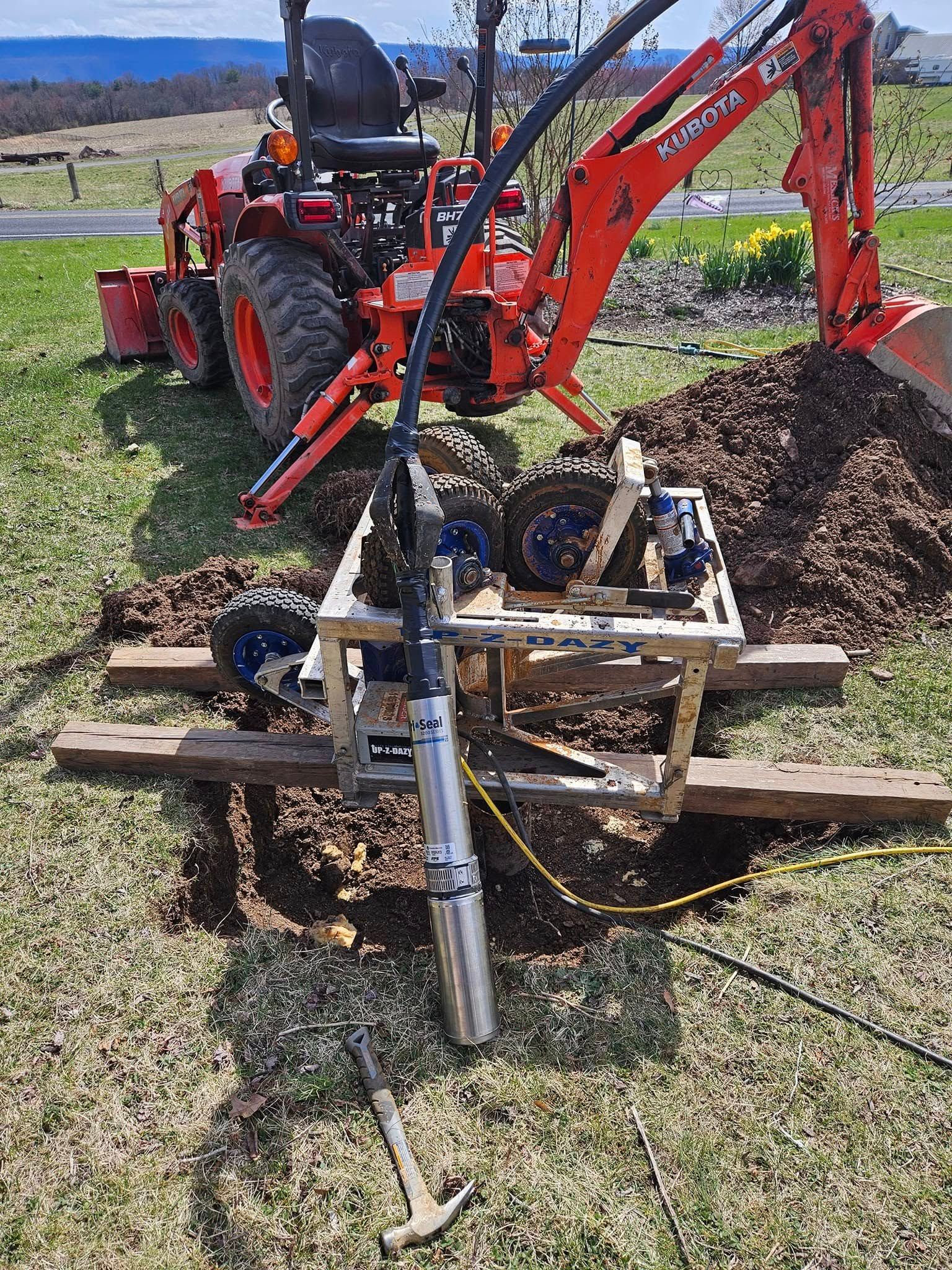 Tractor with backhoe and well-drilling equipment set up to dig.