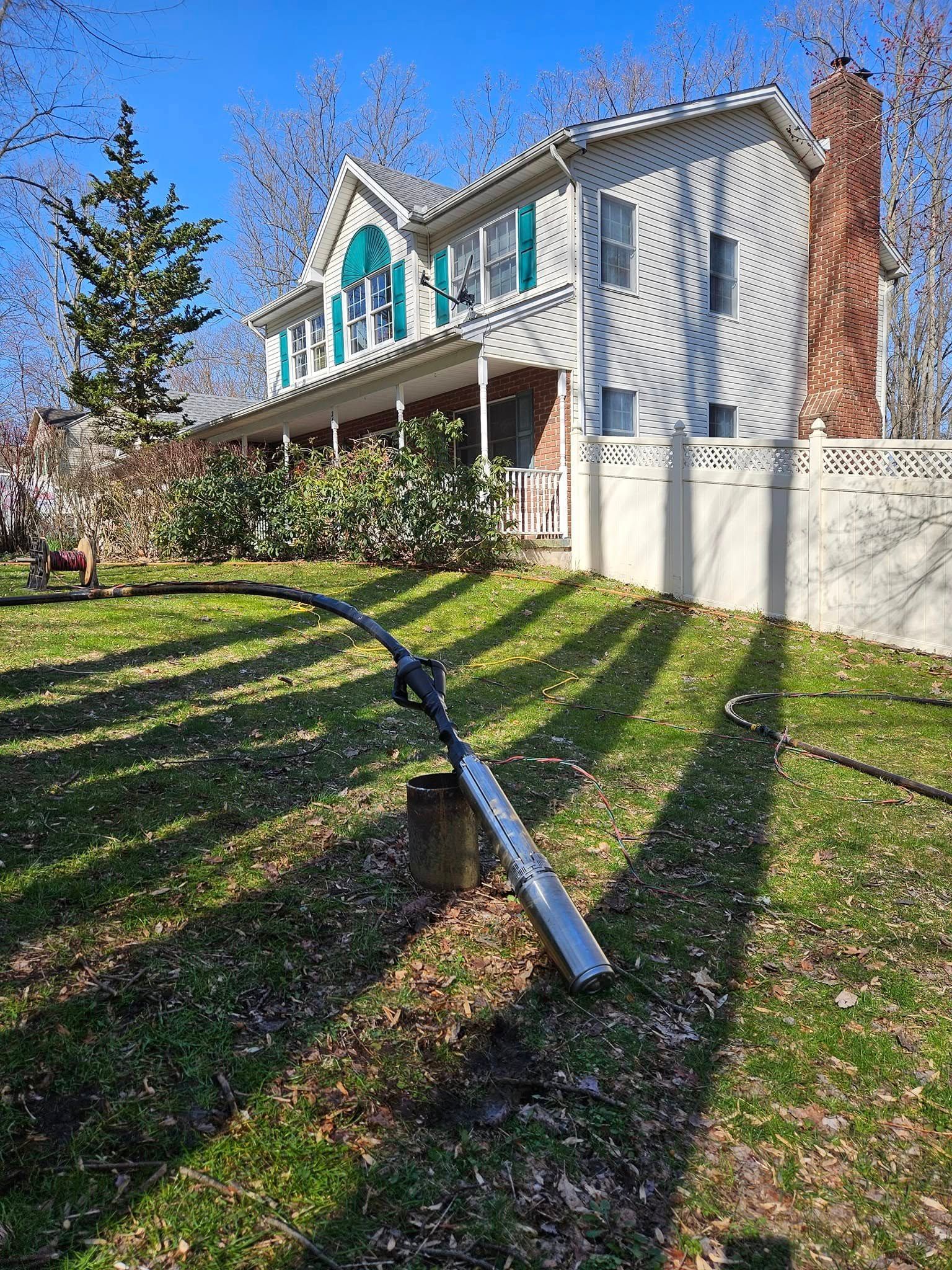 A chainsaw rests on a stump in a grassy yard, with a two-story house in the background.