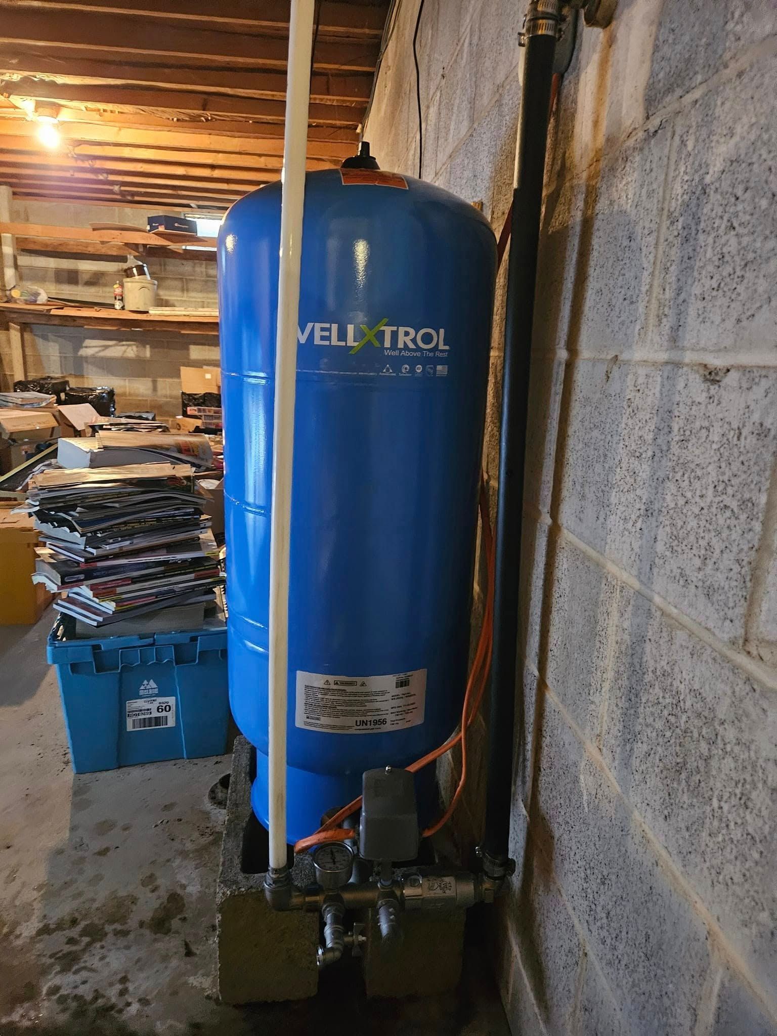 Blue water pressure tank in a basement against a concrete wall.