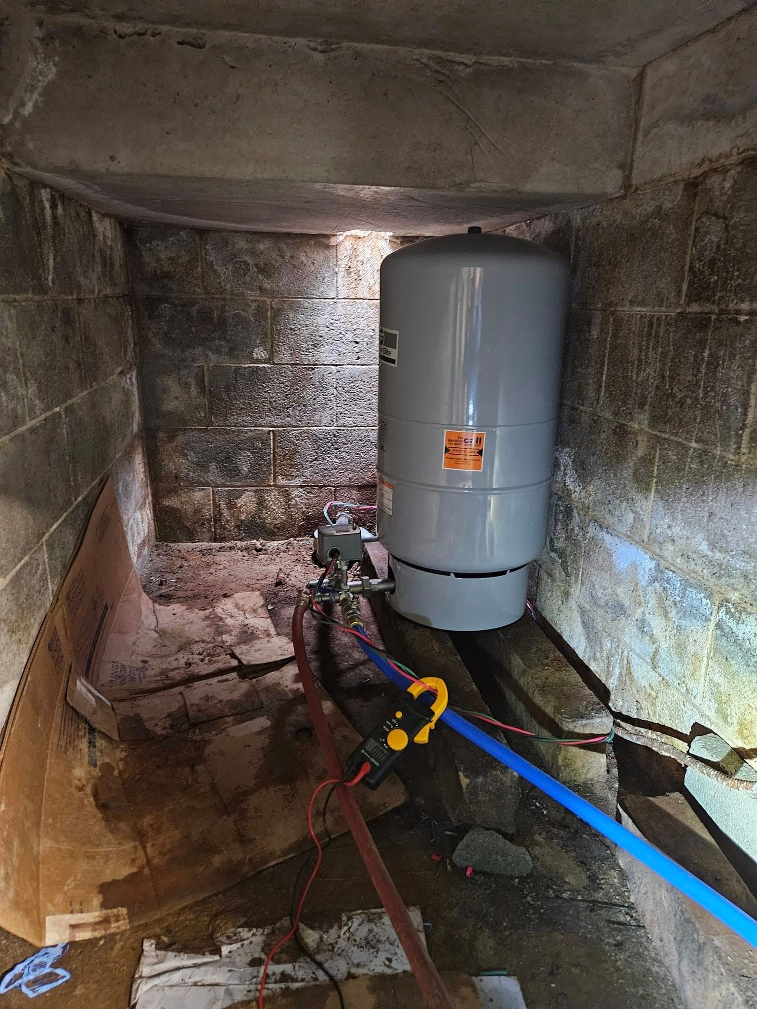 Water pressure tank and pump in a concrete enclosure; blue and red pipes visible.