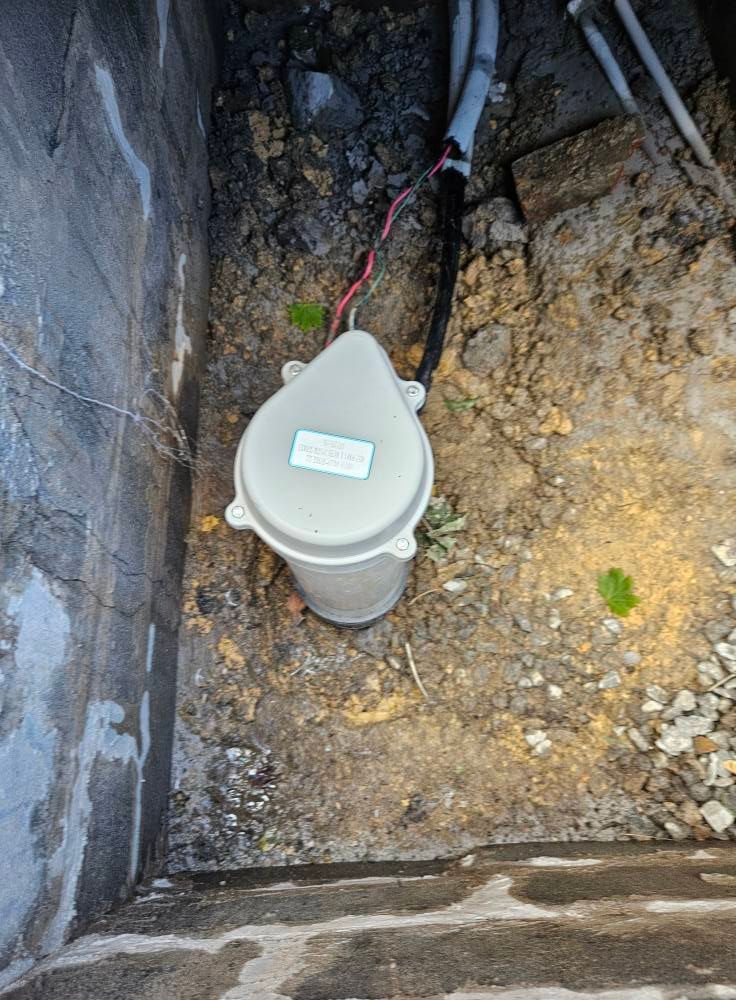 White utility box with wires in dirt near a concrete wall.