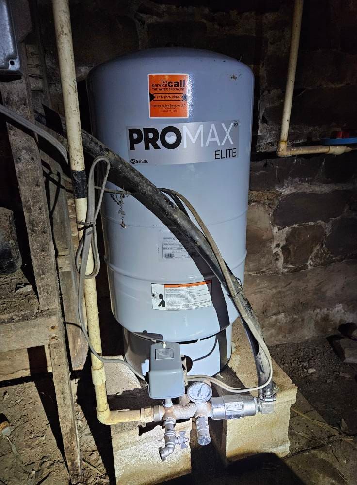A gray ProMax Elite water pressure tank in a basement setting, with pipes and pump visible.