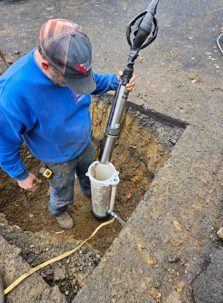 Man using a pump to remove water from a hole in the pavement.