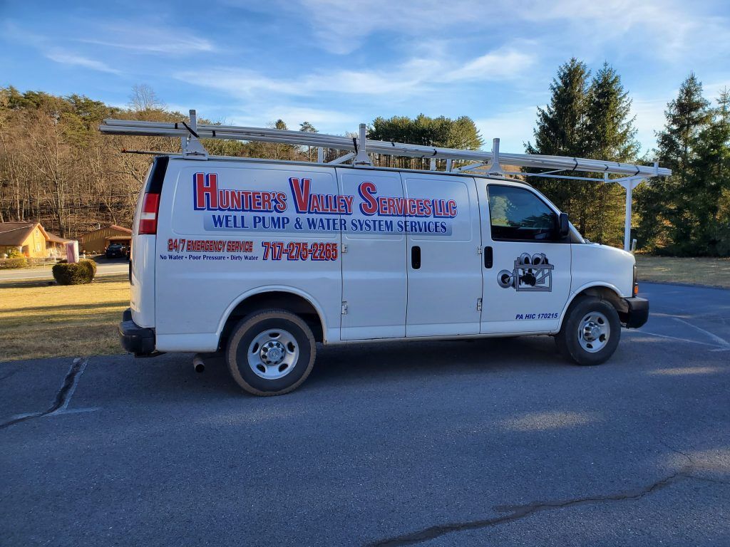 White work van with ladders on roof parked outdoors.
