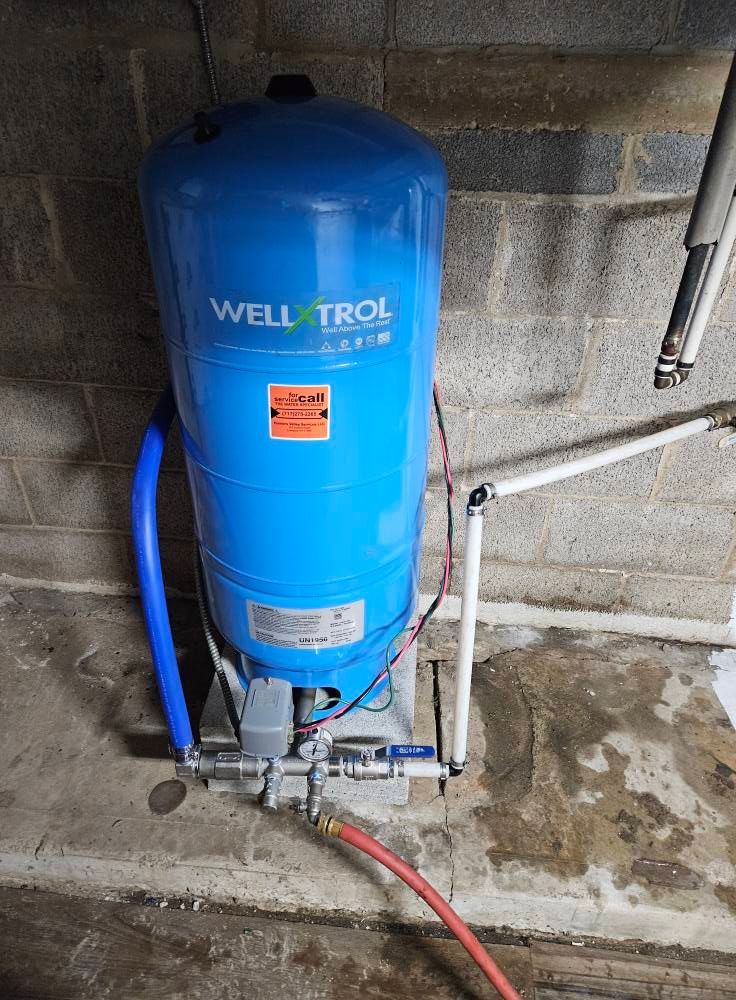 Blue Well-Trol water tank in a concrete room, with attached pipes.