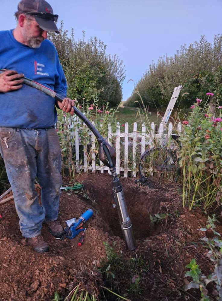 Man operating a pneumatic post driver in a garden, near a white picket fence.
