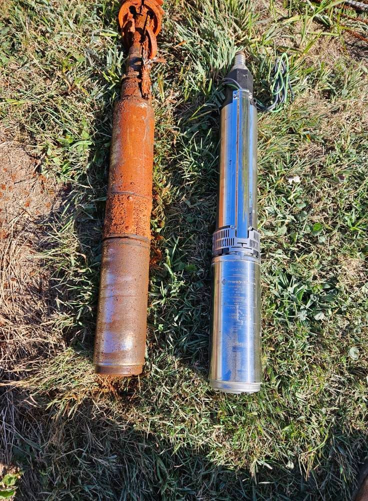 Two well pumps on grass: rusty old one next to a new, shiny one.