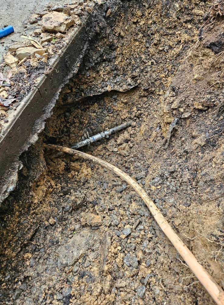 A section of earth dug open, showing a pipe and wire along a concrete edge.