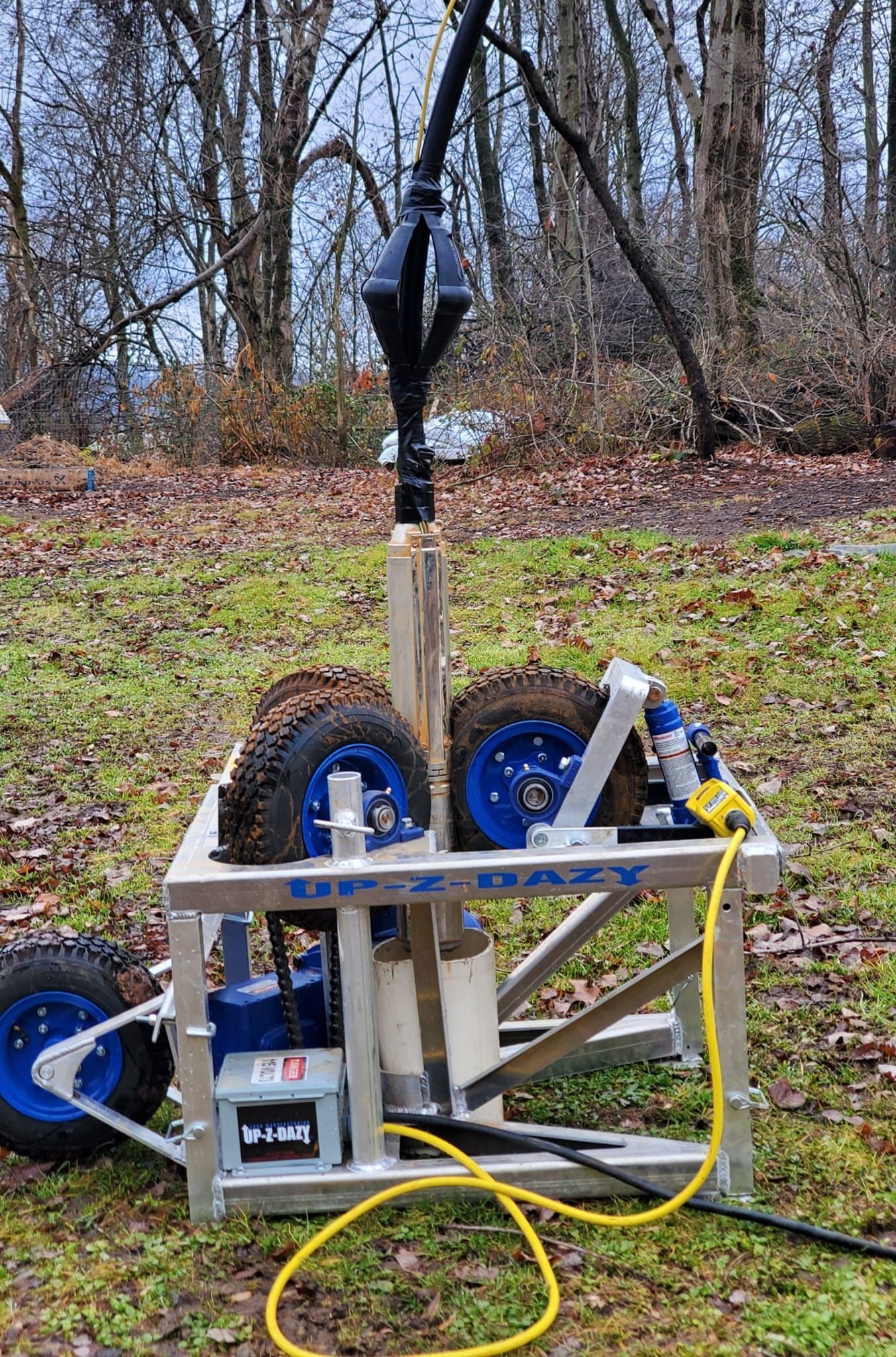 A portable drilling rig with large tires, blue accents, and a yellow power cord, outdoors.