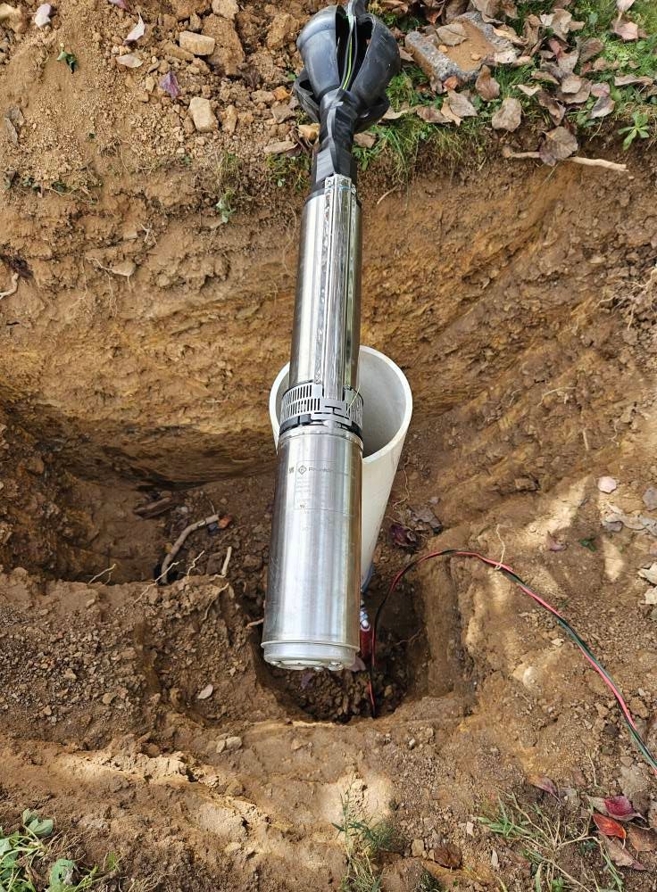 A cylindrical pump and pipe in a soil pit. The pump is silver and black, with wires visible.