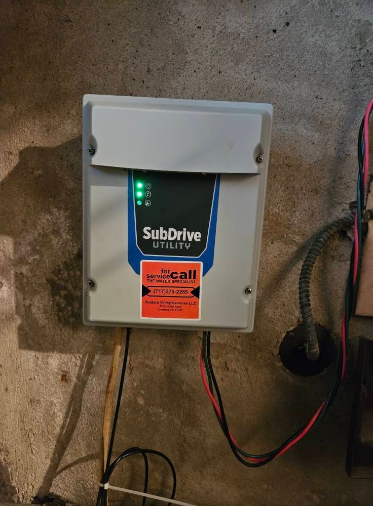 Gray SubDrive Utility control box mounted on a concrete wall. Wires connect to it. Two green lights visible.