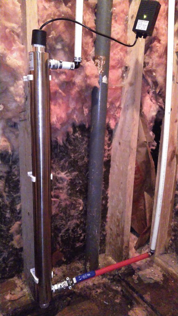 UV water purification system installed against a wooden wall in a basement.