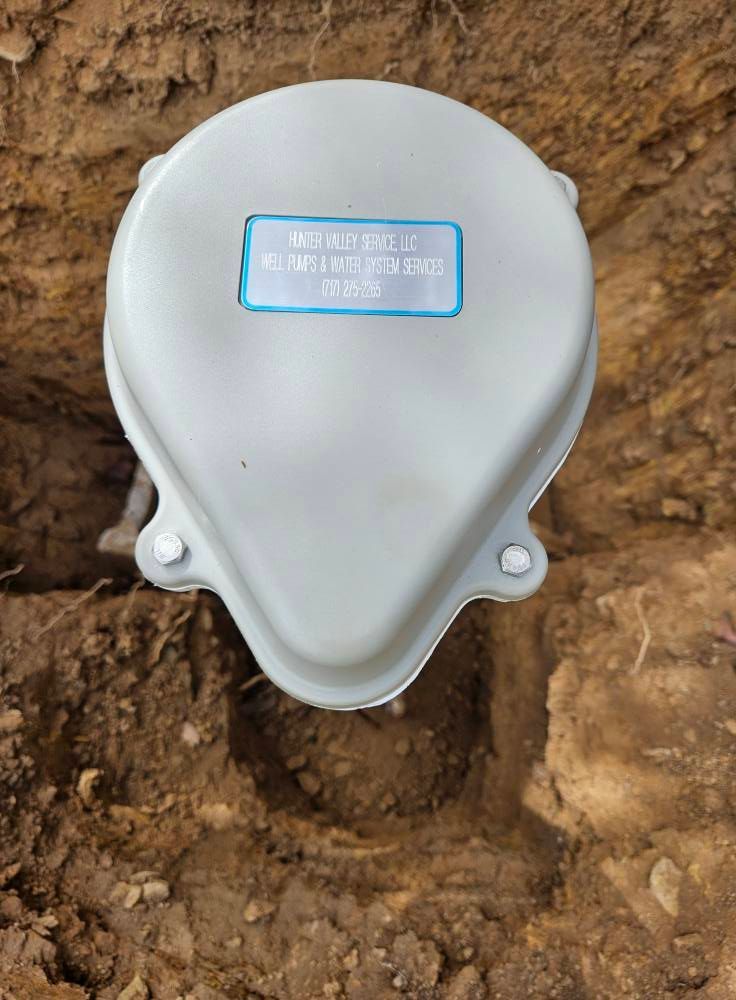 Gray, oval-shaped utility box with a blue label set into a dirt trench.