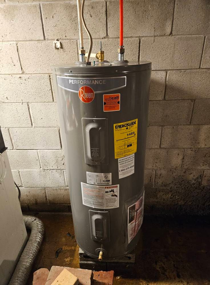 A tall, gray Rheem water heater in a basement setting, with pipes and brick block wall.
