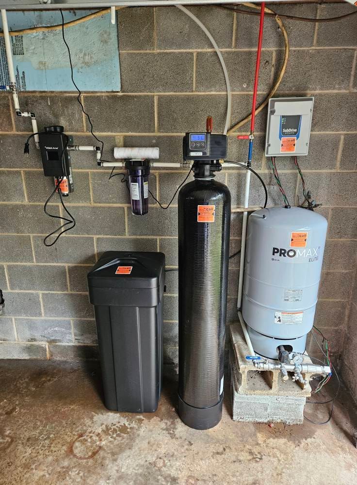 Water filtration and softener system installed on a cinder block wall, with various components and pipes.