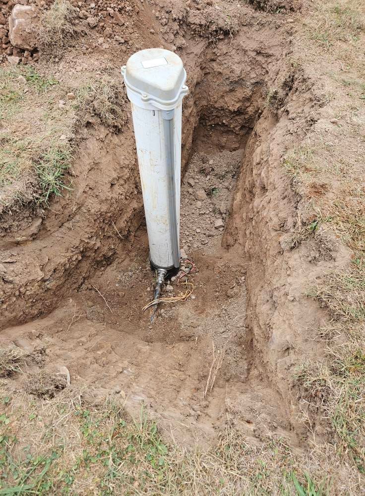 White PVC pipe in a rectangular trench in dirt, with a gray cover.